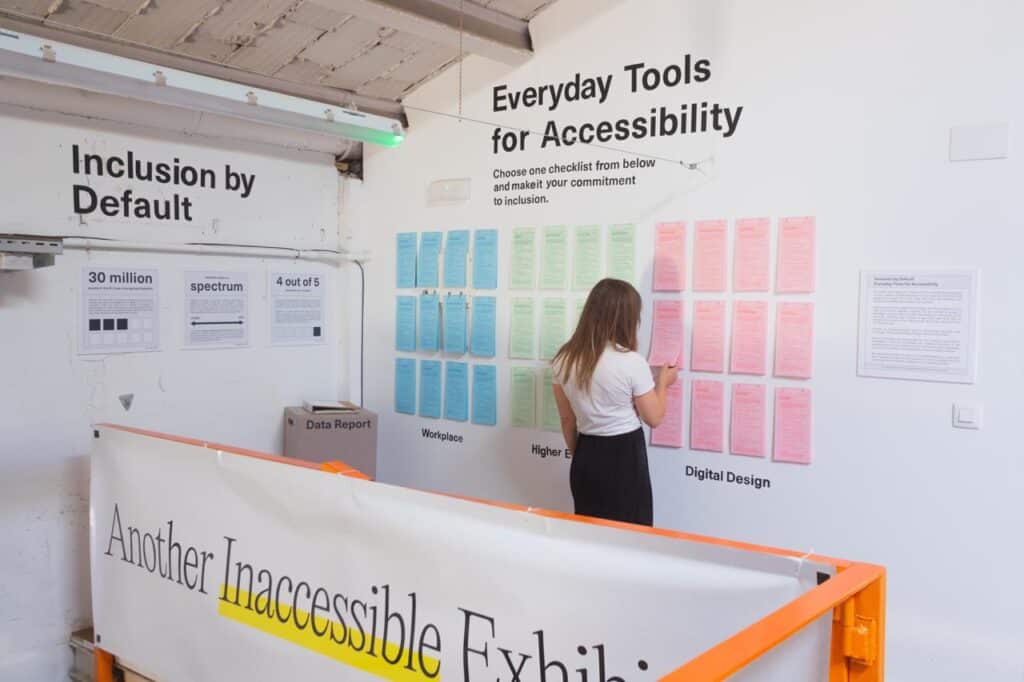 Inclusion by Default: Everyday Tools for Accessiblity. Stack of checklists hanging on a wall person is taking one